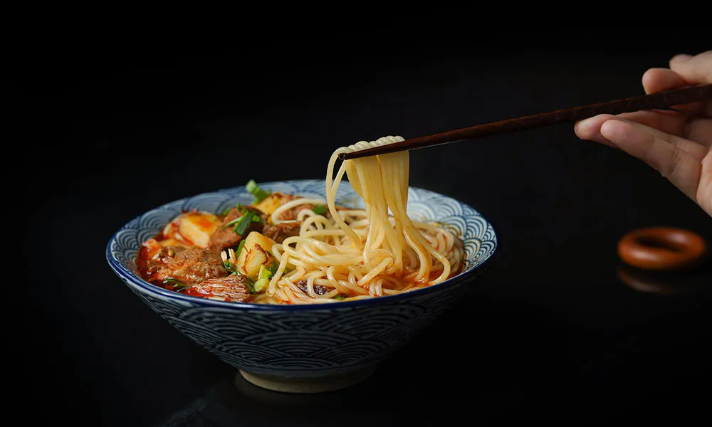 Braised beef noodle soup with hand-pulled noodles being lifted by chopsticks at Sumo Ramen CO, a Chinese Restaurant in Fayetteville
